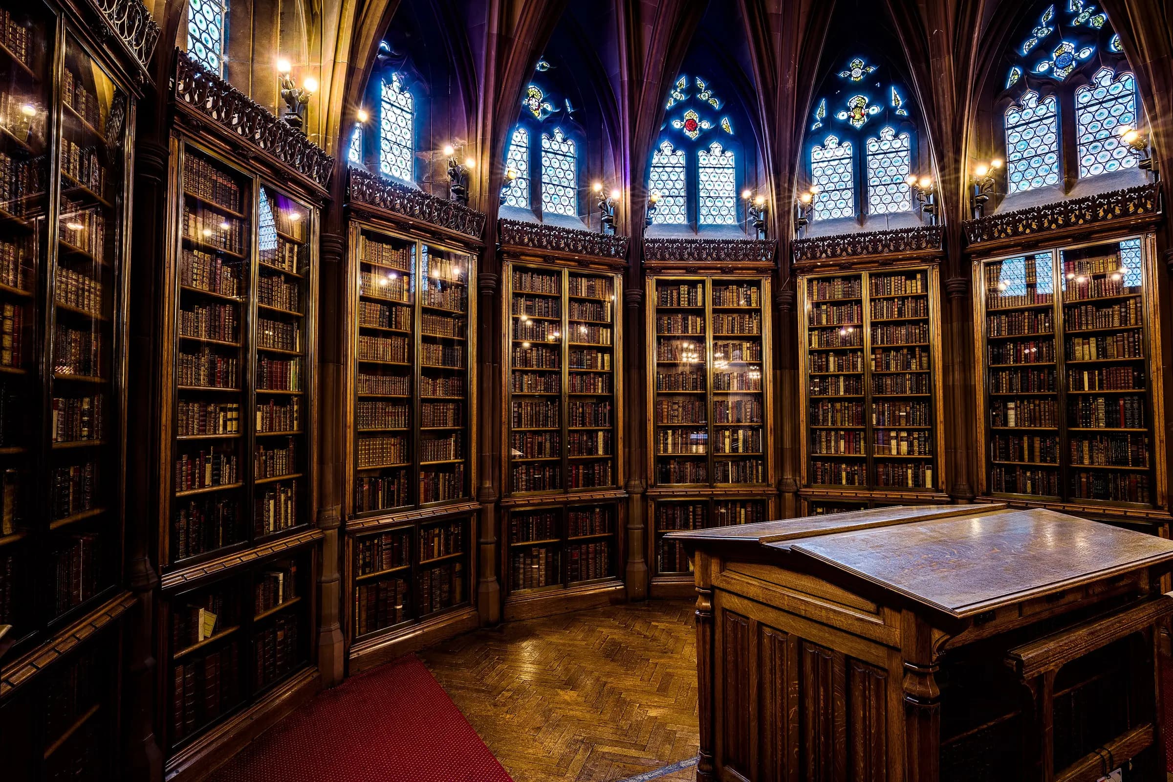 A Gothic reading room lined floor to ceiling with dark wooden bookcases under arched windows
